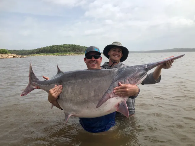 Two men proudly display a large fish while standing in the water, showcasing their successful catch.